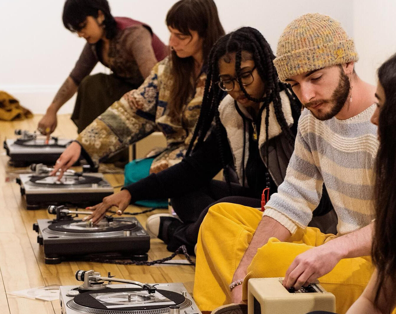 Six Turntables workshop at The Music Gallery (2023) - photo by Kevin Jones 5 young artists sit cross-legged on the floor of The Music Gallery improvising using amplifiers and turntables with flexi-discs